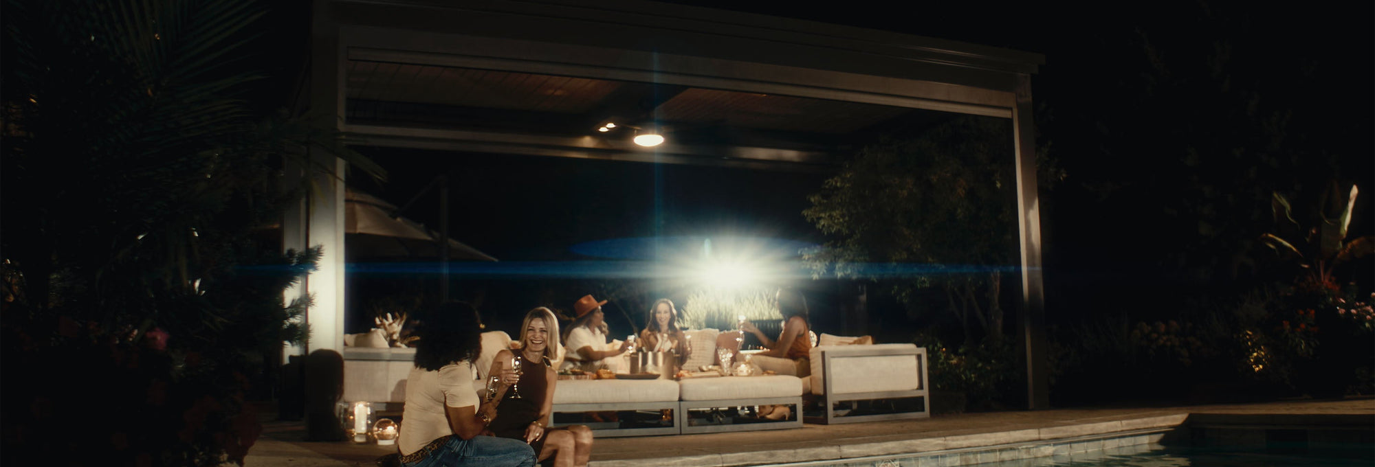 People sitting by a pool at night with a well-lit house in the background