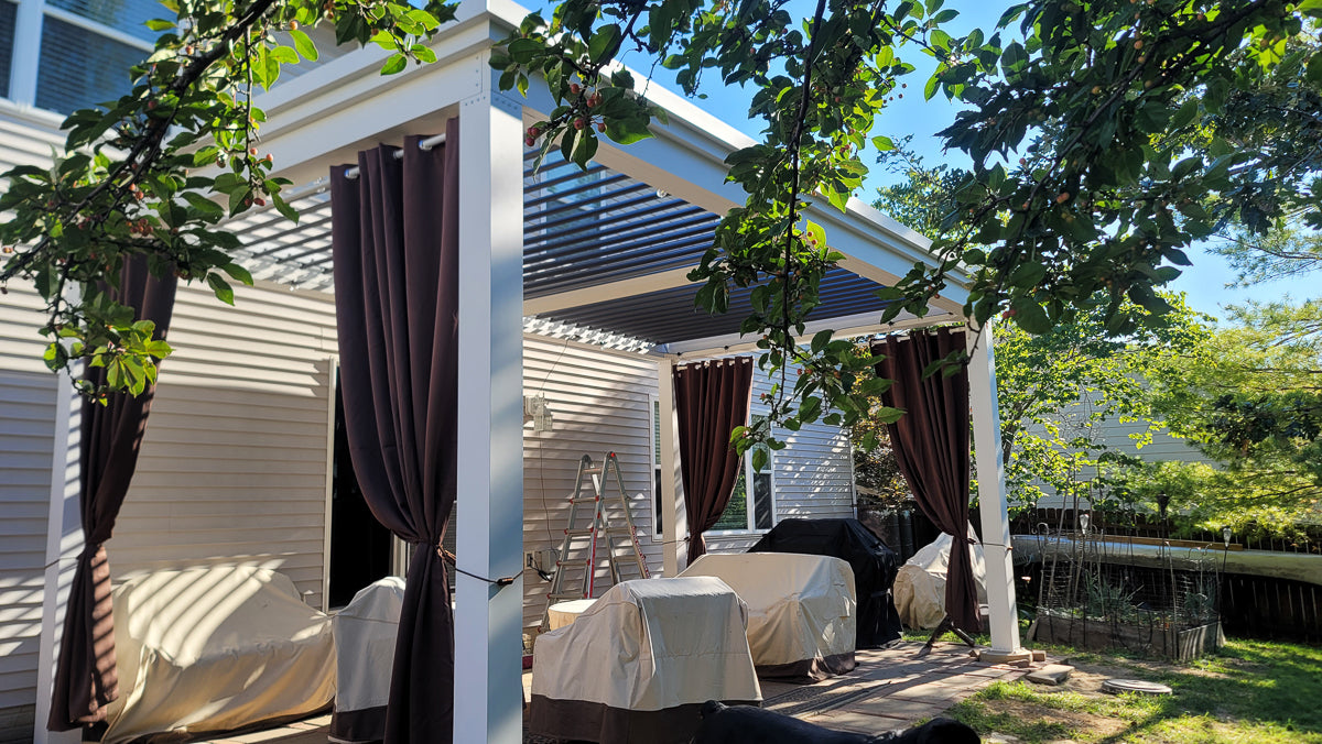 white aluminum pergola structure with curtains and a louvered roof in an outdoor living space.