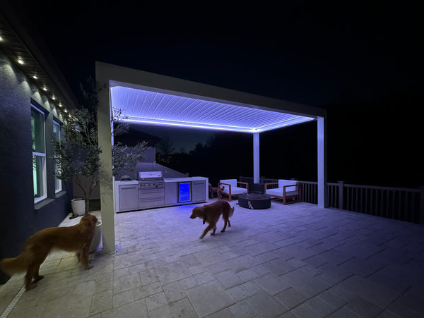 Black pergola with built-in kitchen and LED lighting over patio at night