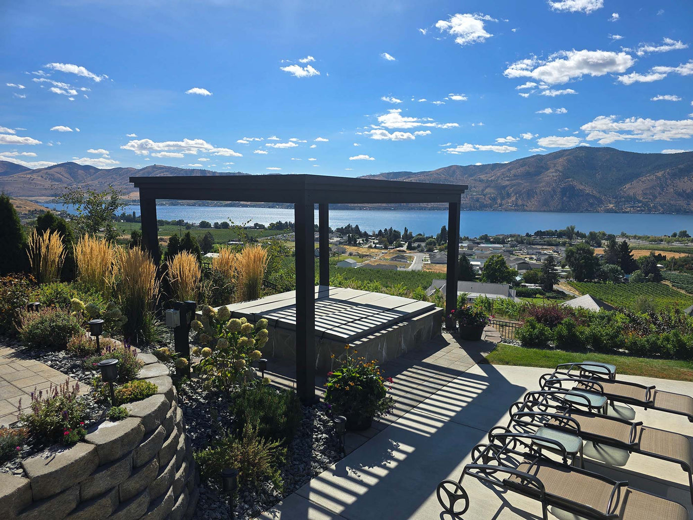 Black pergola with slatted roof on hillside overlooking lake and mountains