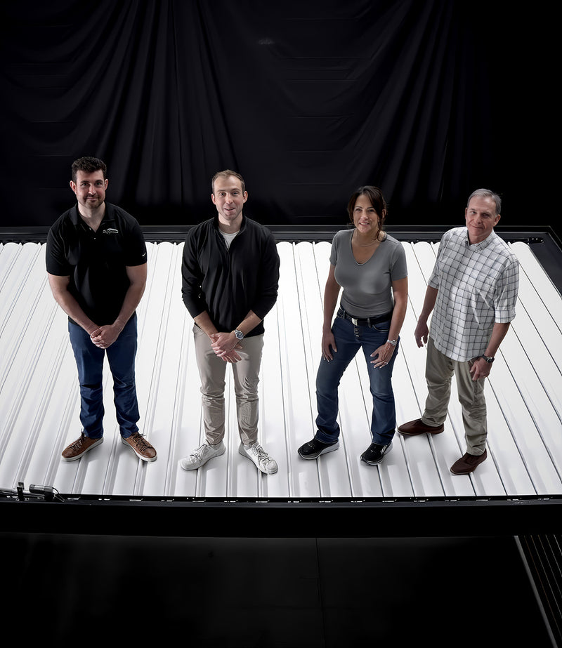 Four people standing on a white platform with a black curtain background