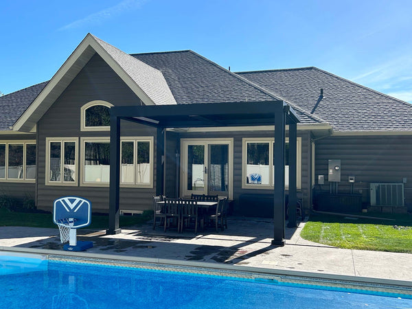 Black pergola over curved patio next to farmhouse