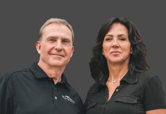 Two people wearing black shirts with logos on a gray background