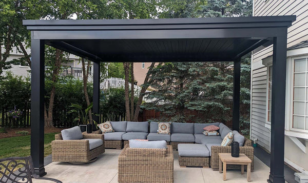 Black aluminum louvered pergola over outdoor lounge seating with gray cushions and wicker furniture