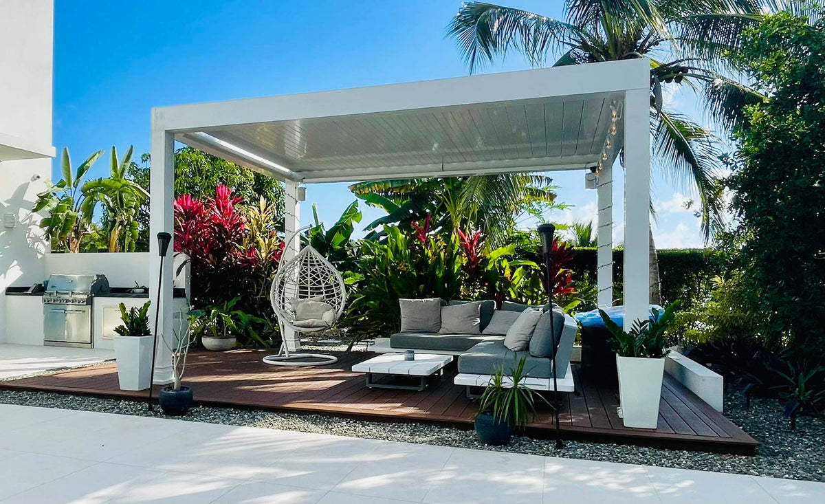 White aluminum louvered pergola over seating with tropical plants and hanging egg chair