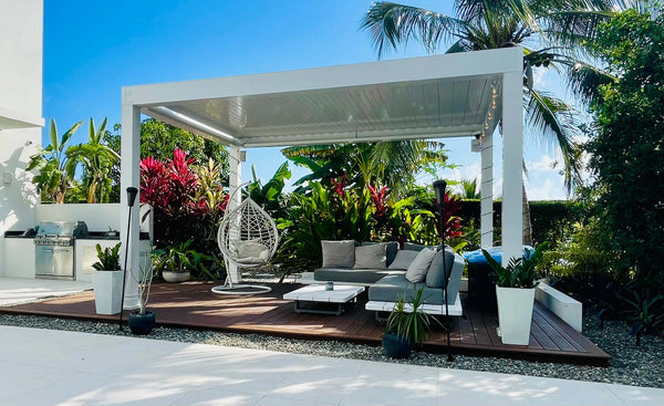White aluminum louvered pergola over seating with tropical plants and hanging egg chair
