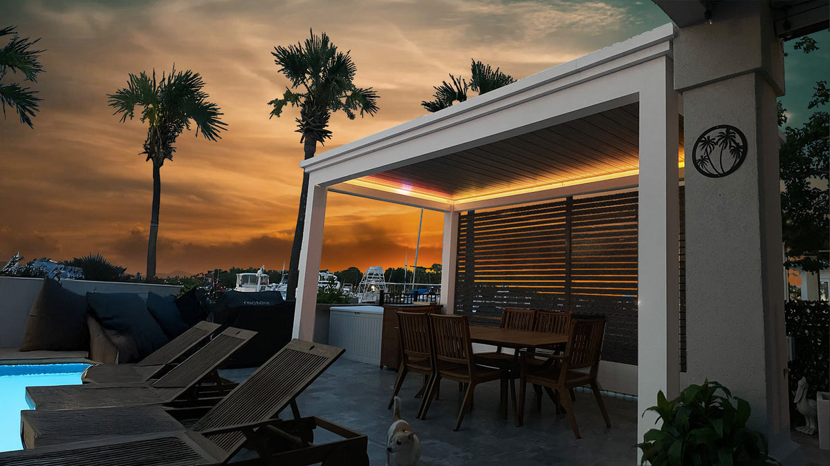 Motorized pergola with LED lighting at sunset, white aluminum frame, black louvered panels, dining setup