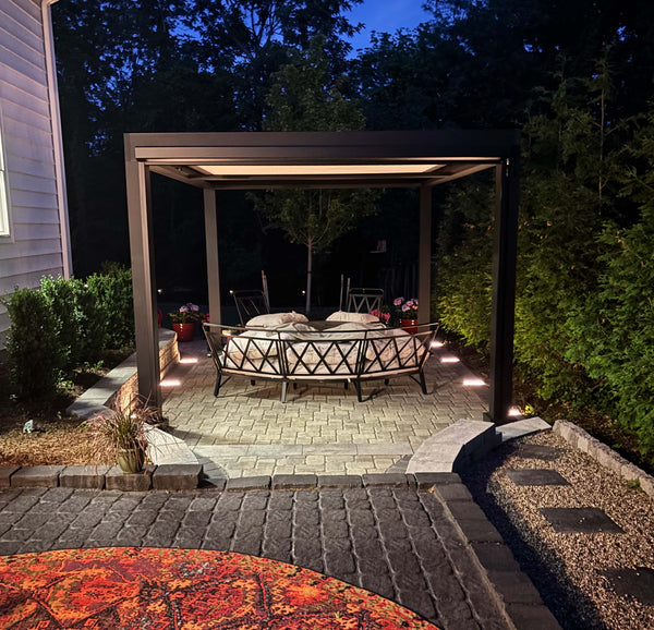 Black aluminum pergola with motorized louvers and brown outdoor curtains over nighttime seating area