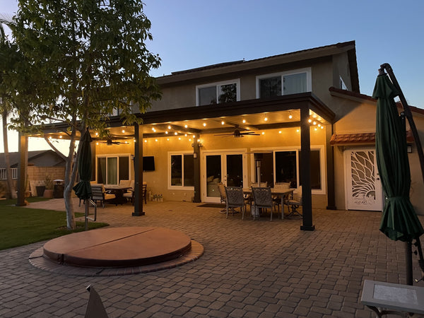 Black metal pergola with slatted ceiling over patio with fire pit and landscaping
